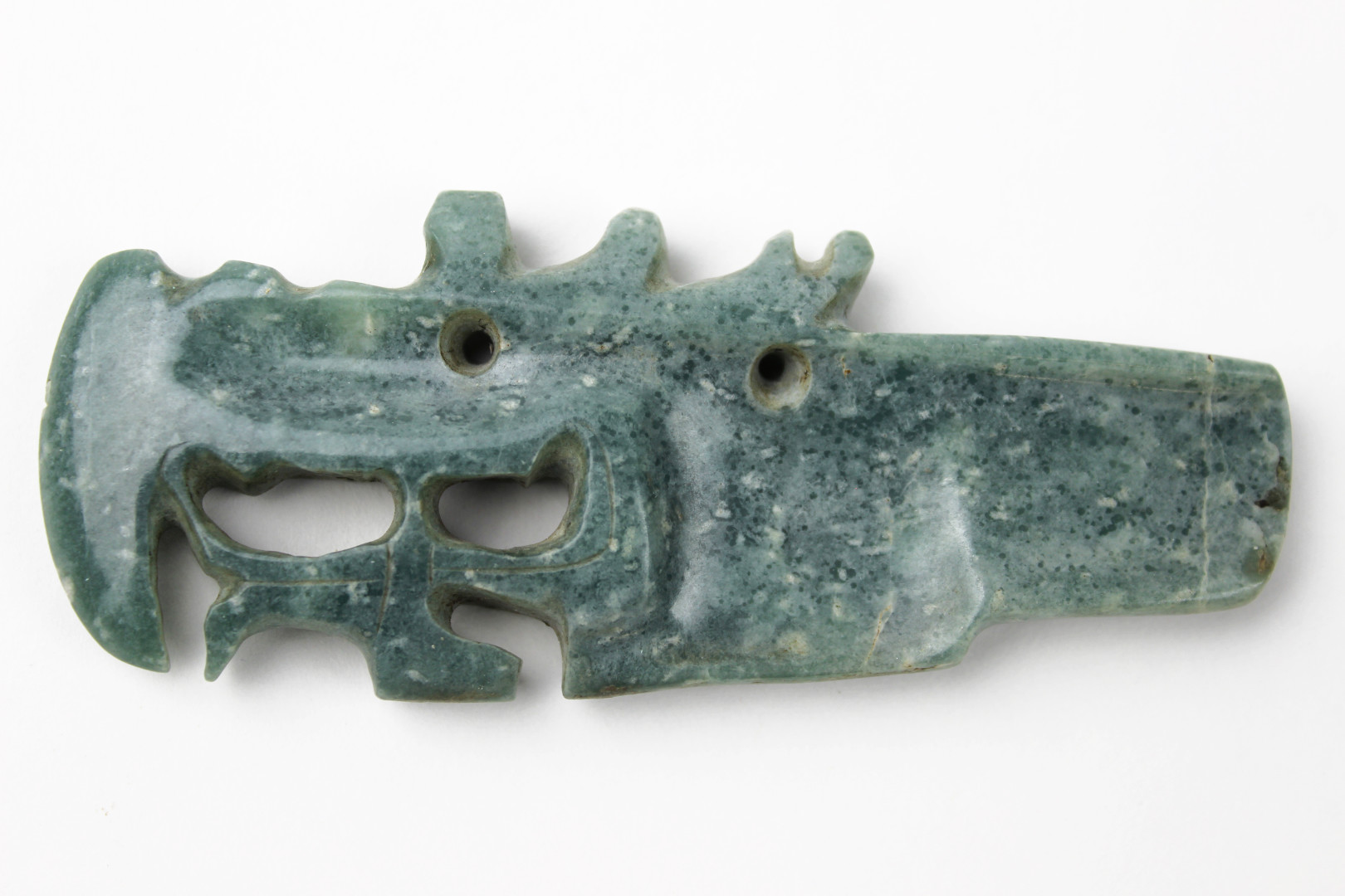 A greenstone sculpture of a creature in profile. The edges and grooves detailing the facial features are worn.