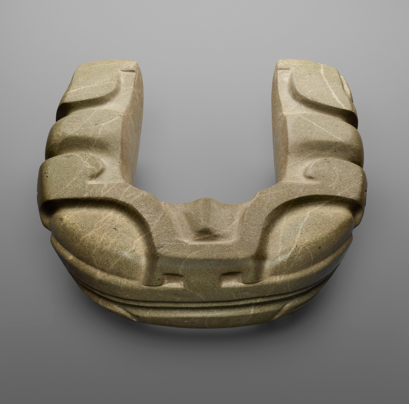 A U-shaped stone sculpture with decorative carvings. The carvings give it the appearance of a frog face.