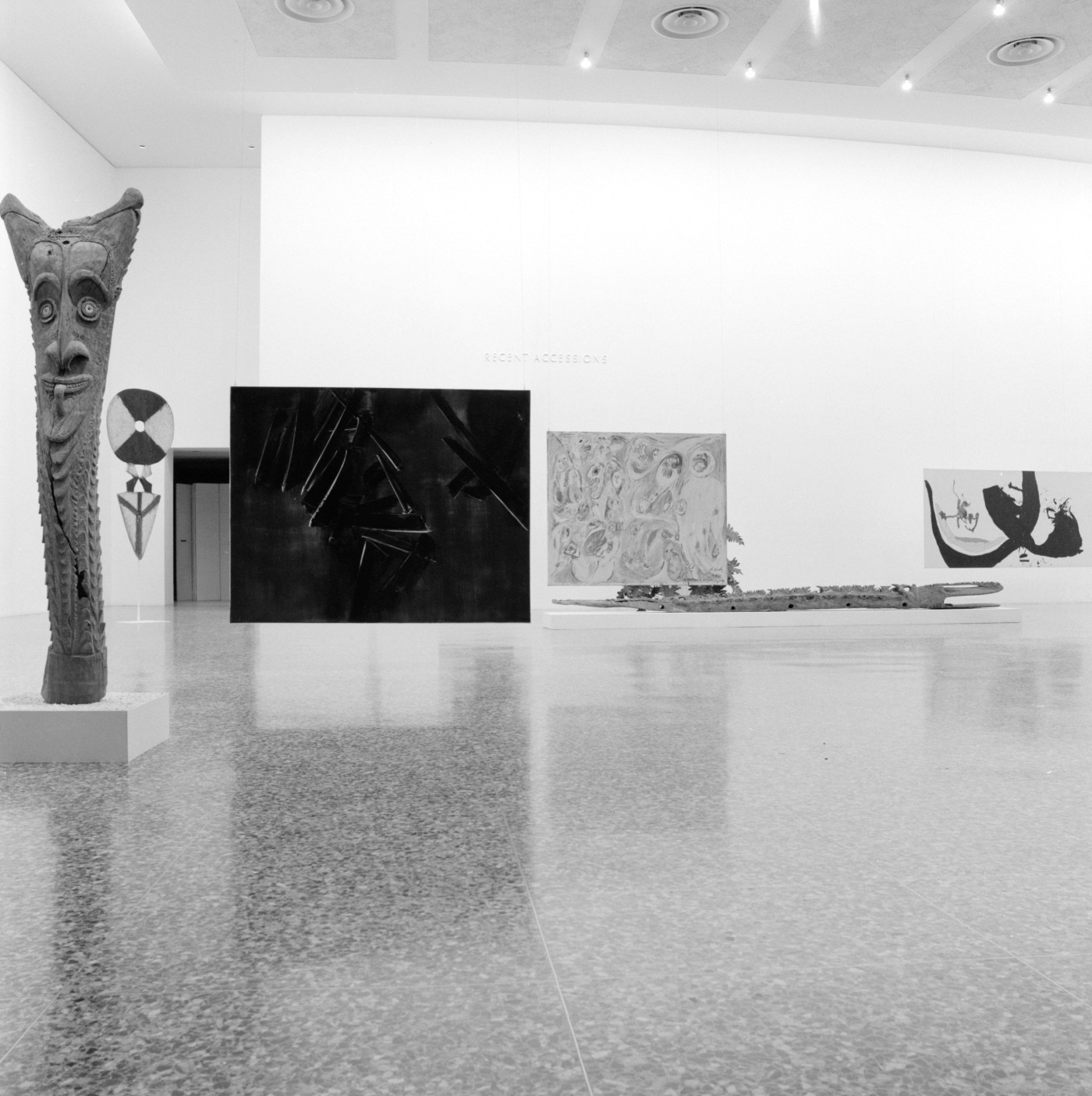 A black and white photograph of large paintings and sculptures in a hall with polished stone floors and neutral painted walls.
