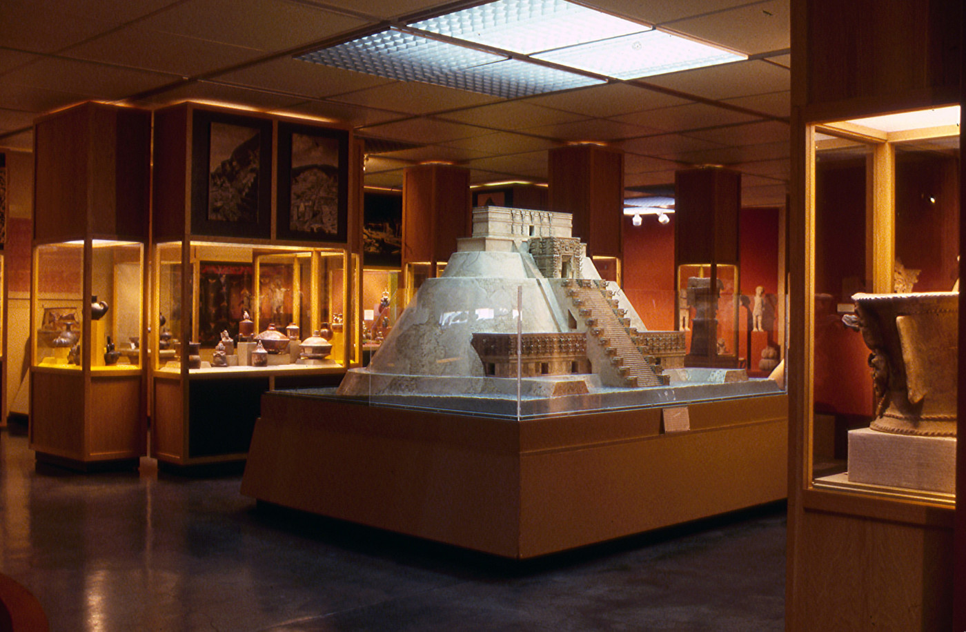 A color photograph of a gallery with a large pyramid maquette in the center. Cases that extend to the ceiling and hold ceramic objects fill the rest of the gallery.
