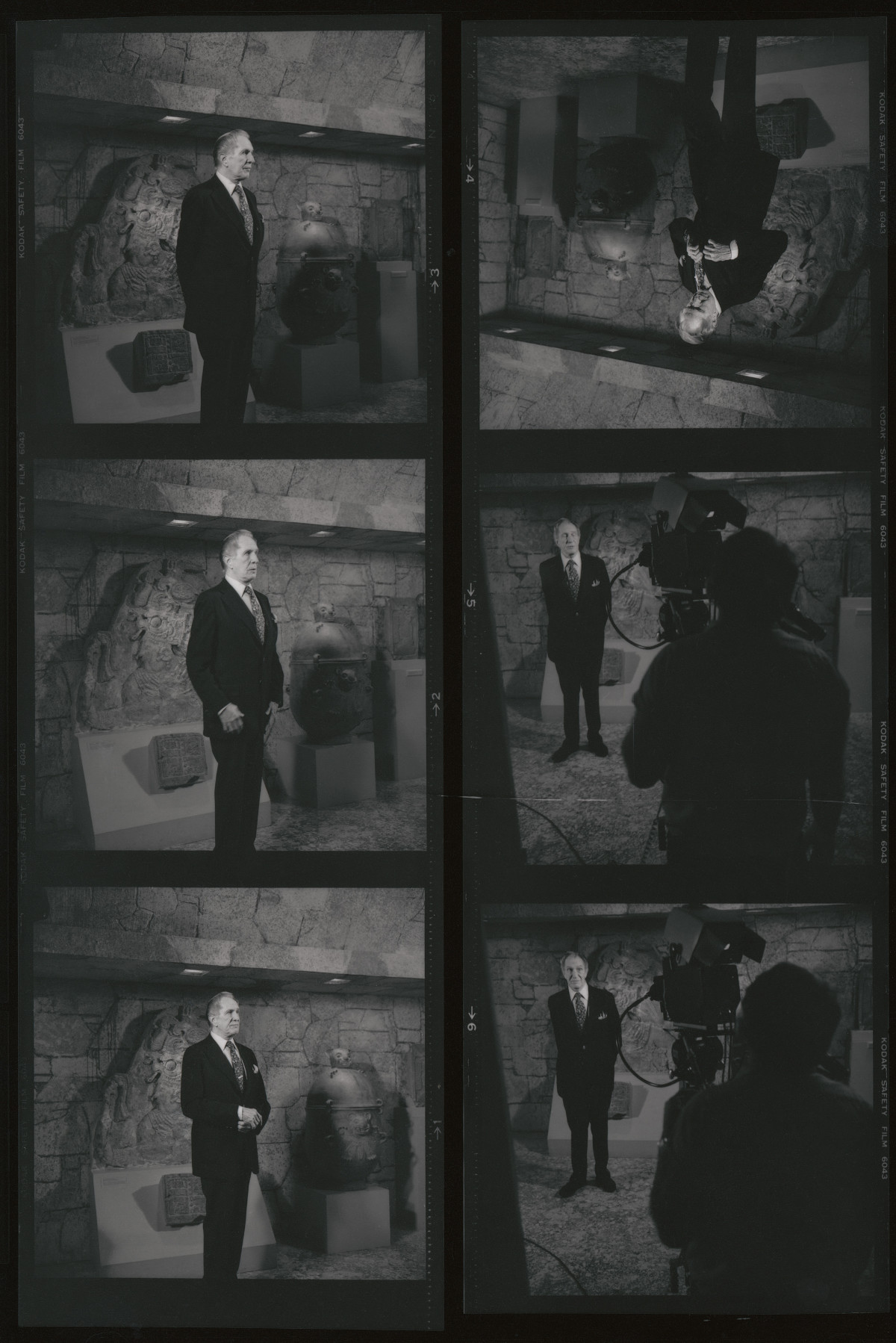 A contact photo sheet of a man in a dark suit standing in a room themed like a stone tomb. There are stone and ceramic sculptures behind him. A cameraperson can also be seen in some of the frames.