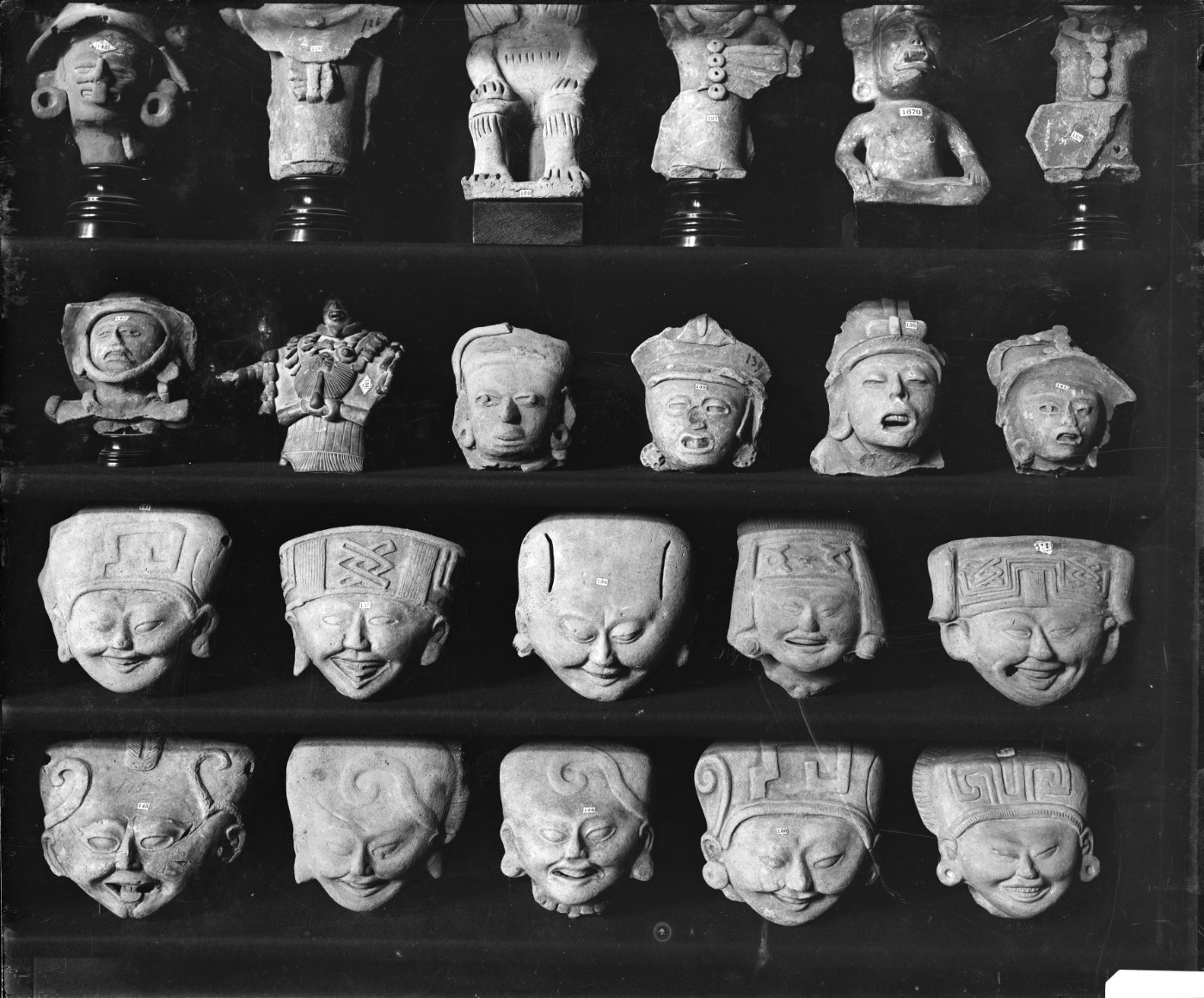 A black-and-white photograph of a display case featuring four rows of five or six small ceramic figurines. All but five of the ceramics are smiling faces.